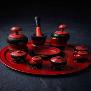 صينية جرتق سودانية تقليدية من الخشب المنقوش باللونين الأحمر والأسود، تضم مبخر وعلب بخور وعطور تراثية بتصميم يدوي فخم على خلفية داكنة.